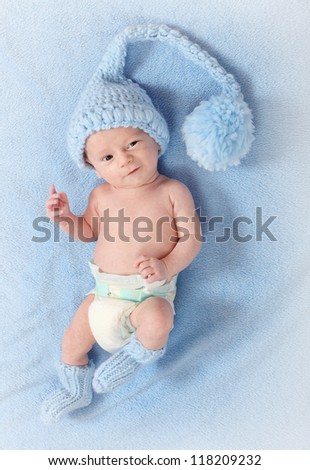 Fashion photo of a cute baby with funny knitted hat and socks for cold weather lying on a blue background.