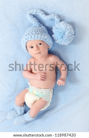 Funny picture of a cute baby with warm knitted hat and socks for cold weather lying on a blue background.