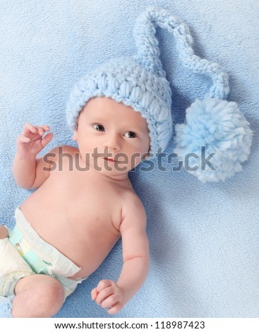 Funny picture of a cute baby with warm knitted hat for cold weather lying on a blue background.