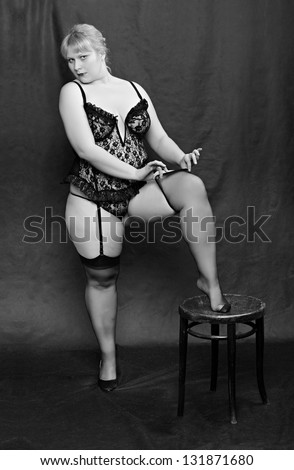 Vintage style picture of an seductive woman dressed in black lingerie posing on a black background.