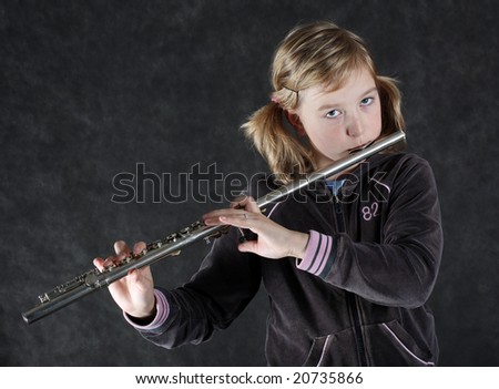 Attractive young girl flautist, flutist holding flute. Studio shot, black background.