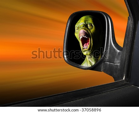 Rear view mirror reflecting fearful monster face - road safety metaphor - green wooden head is unauthorized homemade work.