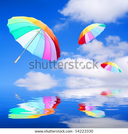 Three rainbow umbrellas flying in a rich blue sky over sea. Conceptual image. Happy holidays metaphor.