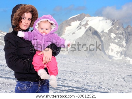 Young highlander with her baby dressed in a fur in snowy mountains. Seasonal fashion shot.