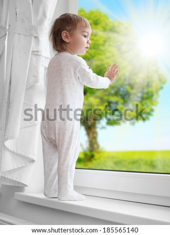 Little boy looking at rural garden from a window. Environmentally friendly living concept.