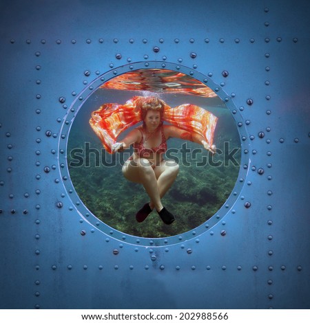 Beautiful woman dancing underwater. Submarine window with view to sea.
