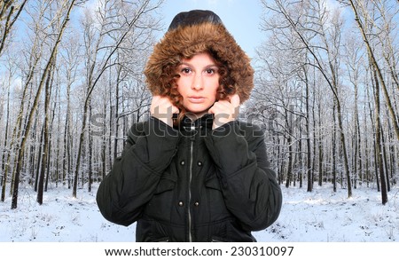 Young woman dressed in warm jacket with fur hood for frosty weather walking in snowy forest.