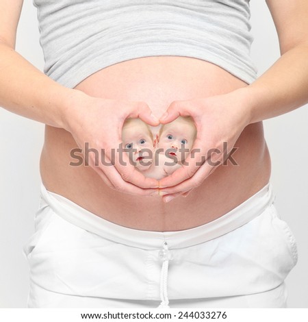 Love and new life. A woman\'s hands forming a heart symbol with twins on her belly.