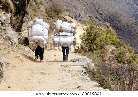 Two sherpa porters carrying heavy sacks in the Himalayas at Everest Base Camp trek ,Nepal.Sherpas are elite mountaineers and experts in the Himalaya mountains.