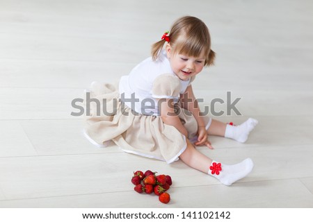 The girl plays with a strawberry on the warm floor