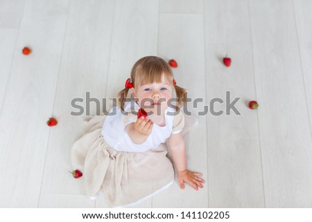 The girl plays with a strawberry on the warm floor