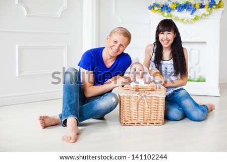 Happy family with a newborn baby in a basket on the floor near the fireplace