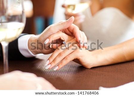The bride and groom are sitting at a table in a restaurant. The groom\'s hand stroking his bride. The bride with a ring, engagement.