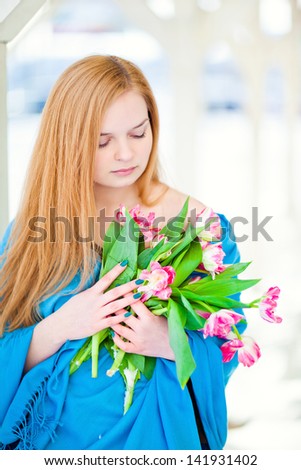 A beautiful blond woman holding a bouquet of flowers. Winter landscape. Snow and wind.