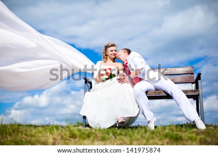 The bride and groom sit on the bench. Veil in the wind.
