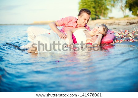 The bride and groom in their wedding clothes lie in the water of the sea. Trash the dress. After the wedding. Fun, romance.