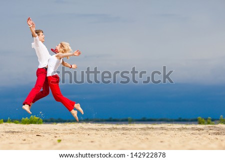 A man and a woman, jump towards each other. Lovers, honeymoon, family look. Beautiful young couple on the beach. Loving couple having fun on nature. Love, romance, fun. Red and white clothes.