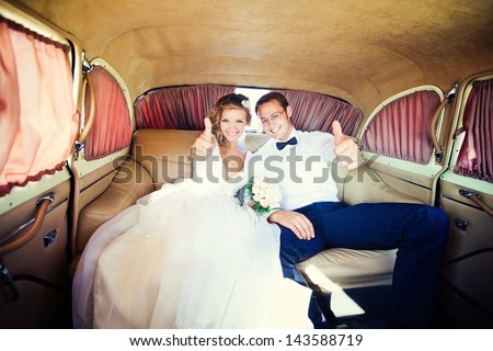 The bride and groom are sitting inside the retro car.