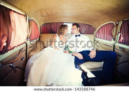 The bride and groom are sitting inside the retro car.