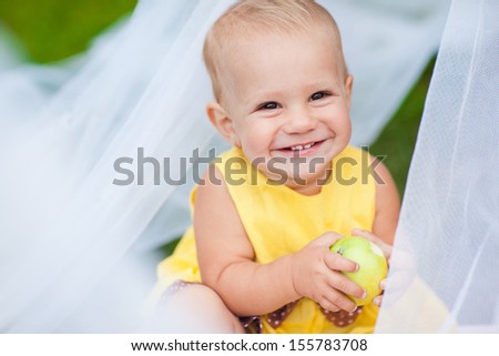 A child holding an apple and smiling broadly. The first teeth a little girl. The first solid food.