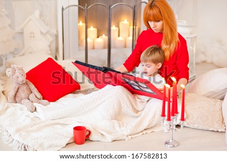Christmas Eve. Mother reading to her son bedtime story. New Year at home with family. Festive decor. Evening by the fireplace.