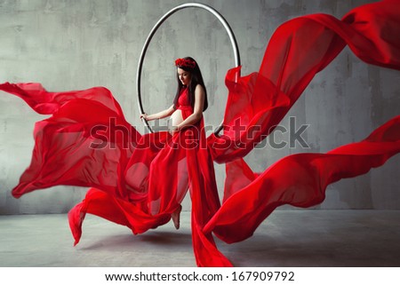Beautiful pregnant woman acrobat in red long dress. Waving fabric. Fashion pregnancy.