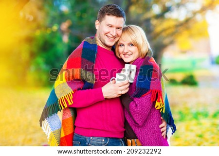 Young beautiful couple embracing under a blanket in the park. Tea party on the nature. Autumn landscape. Love. Relationship. Love as a way out of the autumn depression.