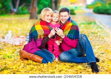 Beautiful family keep warm under a blanket in the autumn park. Fun and games in nature.