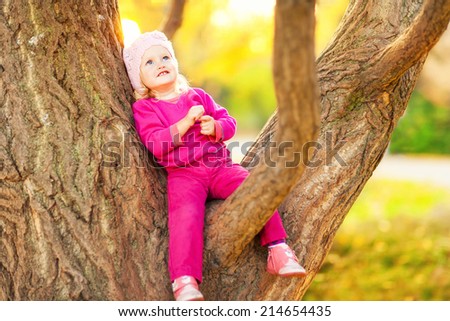 Sweet funny baby girl sitting in a tree in the autumn park