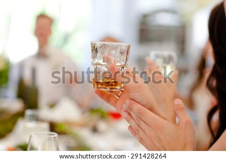 A woman holding a glass of whiskey and applauding at the reception. Toast. Wedding reception. The solemn feast.