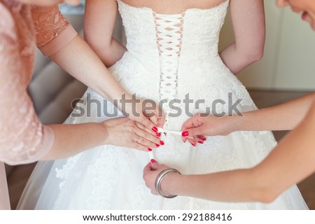Bridesmaid is helping the bride to dress. The bride\'s dress.