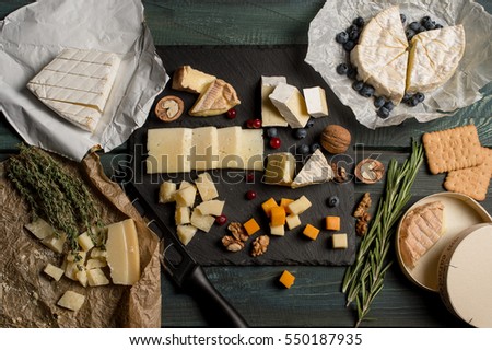 Tasting cheese dish with herbs and fruits on old black wooden table. Food for wine and romantic, cheese delicatessen. Menu design horizontal. Top view.