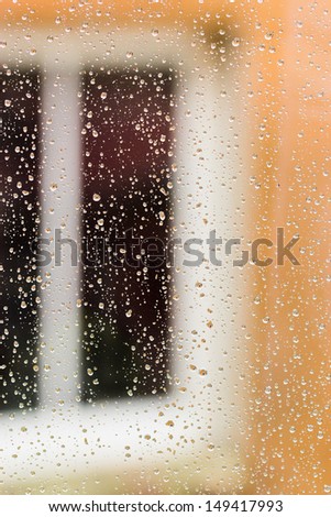 Raindrops on glass with reflections of big window from the background. Selective focus on raindrops.