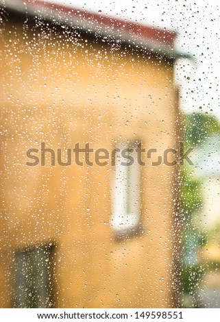 Wet glass with raindrops. In the background part of house with two windows