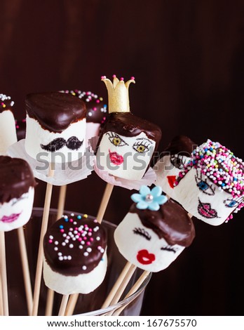 Funny marshmallow pops with hand-painted faces. Decorated with dark chocolate and sugar sprinkles. Selective focus