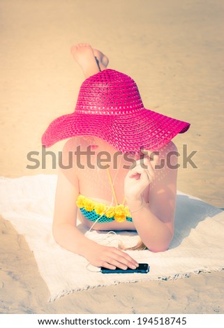 Young girl  on the beach protecting her very white skin with a big pink hat and hearing music. Selective focus on hat and hands. Toned image.