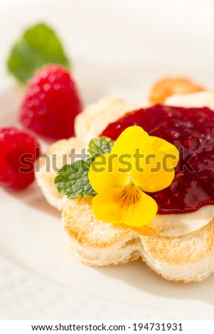 Breakfast: crispy toast in flower shape with butter and raspberry jam. Decorated with yellow pansy flower and mint leaf. Selective focus.