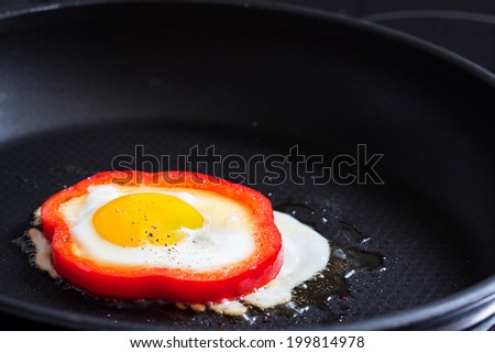 Fried egg in red pepper ring on a black pan. Selective focus