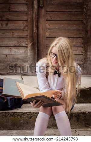 Blond school girl with nerd glasses reading a book. Selective focus.