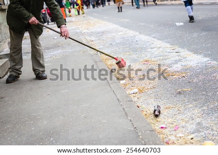 Old man sweeping the street after a carnival party. Selective focus.