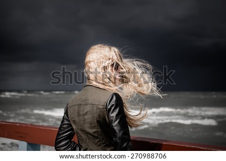 Blond girl looking at stormy sea. Dark sky in in the background. Selective focus.