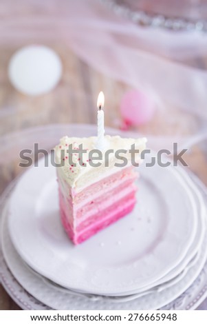 Piece of a pink and white birthday cake with one burning candle. Selective focus. Top view.