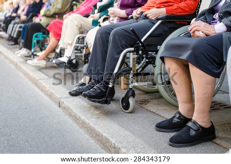 Row of old people in wheel chairs on the sidewalk. Selective focus