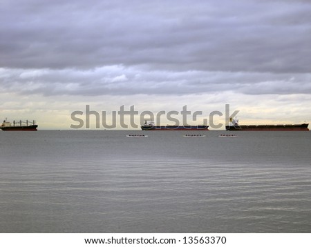 Tanker cargo ships and racing boats on the horizon under an overcast sky