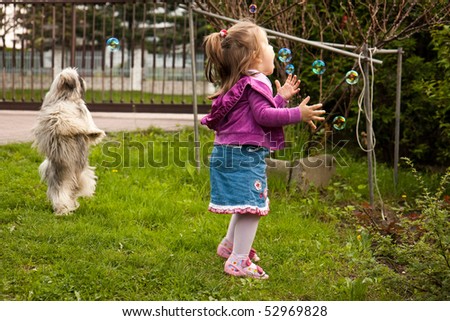 Girl and dog playing with soap bubbles in the garden