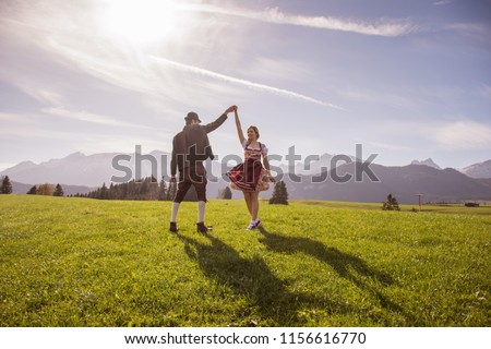Young couple in traditional bavarian clothes with girl in dirdl dress dance in nature / Bavarian Couple Dance Oktoberfest Munich