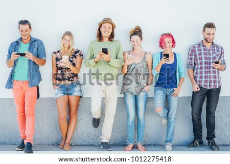 Young people watching on their smart mobile phones leaning on a wall - Generation addicted to new technology - Concept of youth addiction to social network trends
