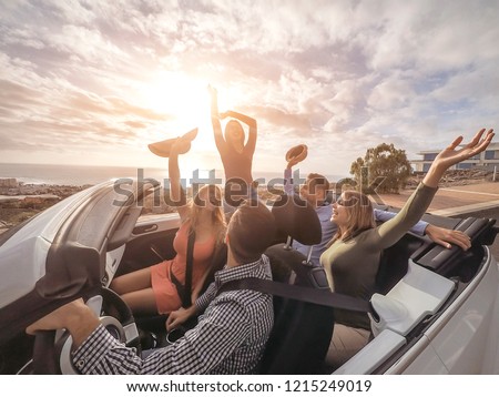 Happy friends with their hands up having fun in cabriolet car on vacation - Young people laughing and enjoying together during travel road trip - Youth holidays lifestyle concept