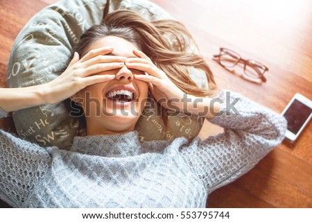 Beautiful young woman laying on the floor laughing with her eyes covered waiting for a surprise - Gorgeous girl covering her eyes with hands dreaming - Soft red light - Focus on the girl\'s hand