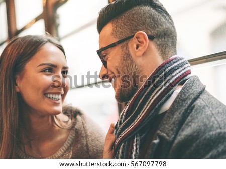 Beautiful happy couple looking at each other\'s eyes traveling on a old vintage tram bus  - Stunning woman smiling to her boyfriend and pulling his scarf - Focus on man eye
